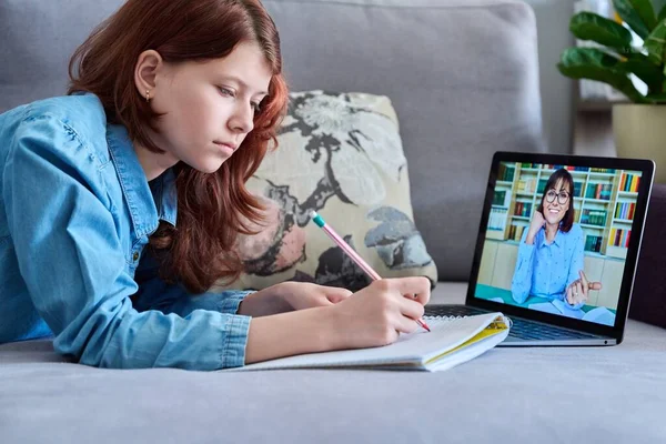 Preteen girl studying at home using a laptop, student watching video lesson course, writing in notebook, teaching teacher on screen. E-education, technology, e-learning, school concept