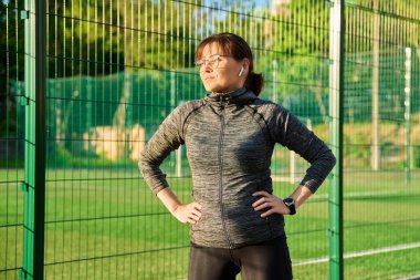 Sportif, olgun bir kadın spor stadyumunda antrenmandan, koşudan ve egzersizden sonra ayakta duruyor. Aktif sağlıklı yaşam tarzı, şehir sporu, orta yaş, insan konsepti