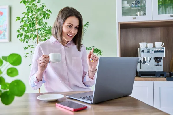 Joyful surprised woman looking at laptop screen, sitting at home in kitchen, with cup of coffee. Surprise, good news, internet, email, social networks, technology, emotions people concept