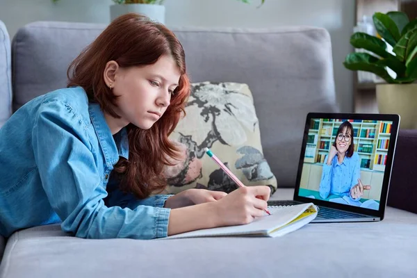 Preteen girl studying at home using a laptop, student watching video lesson course, writing in notebook, teaching teacher on screen. E-education, technology, e-learning, school concept