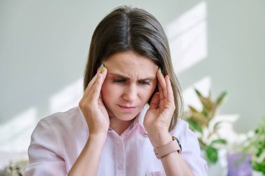 Baş ağrısı olan genç ve stresli bir kadın elleriyle başını tutuyor. Sağlık, migren, depresyon, negatif, sorunlar, insan kavramı