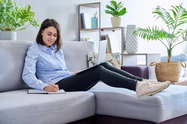 ソファに座ってノートを作るラップトップを使用して自宅から働く若いビジネス女性 フリーランス リモートワーク オンラインビジネス テクノロジー Eラーニング Eラーニングの概念 — ストック写真