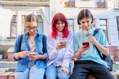 Genç arkadaşlar birlikte şehir sokaklarında akıllı telefonları kullanarak eğleniyorlar. Teknoloji mobil uygulamaları, yaşam tarzı, tatil eğlencesi, şehir tarzı, gençlik kavramı