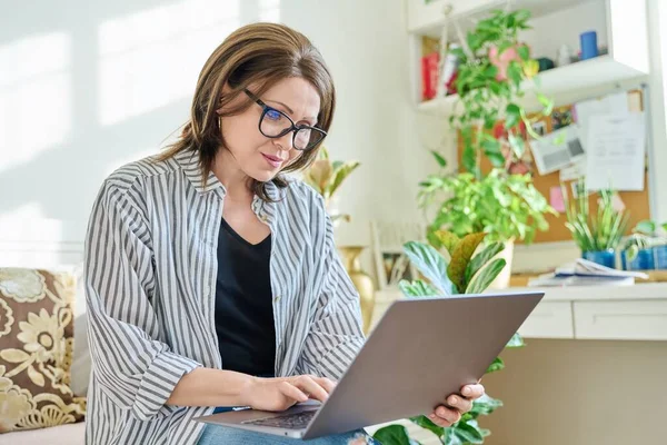 Mature businesswoman working on couch, using laptop. Confident middle aged female working from home office remotely. Business job freelancing, online service, technology, 40s people