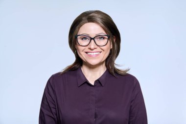 Gözlüklü, gülümseyen bir kadının hafif stüdyo arkaplanındaki kameraya bakışının portresi. Yönetim, personel, meslek, orta yaşlı insanlar konsepti