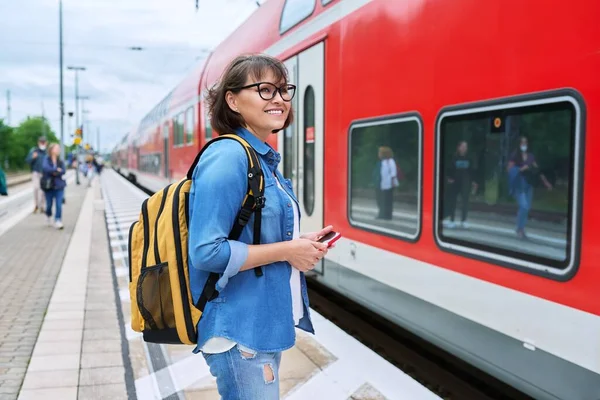 Woman passenger waiting for commuter train at station outdoor platform. Rail transport, passenger transportation, destination, journey, tourism, travel, trip, people concept