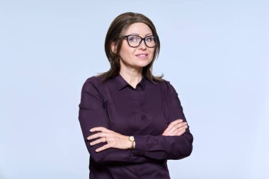 Portrait of confident mature woman in glasses looking at camera on light studio background. Smiling female with crossed arms, dark shirt, hairstyle make-up. Business sales profession staff people 40s