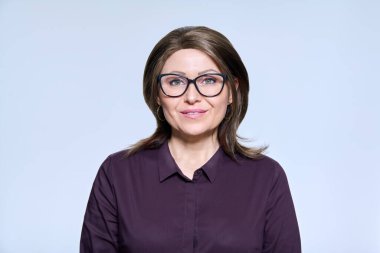 Headshot portrait of a mature smiling woman in glasses looking at camera on light studio background. Management, staff, profession, middle aged people concept