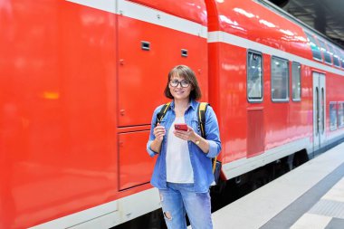 Akıllı telefonlu bir kadın istasyon içinde tren istasyonunda bekliyor. Sırt çantalı bir kadın kameraya bakıyor. Demiryolu taşımacılığı, yolcu taşımacılığı, seyahat turizmi insanları