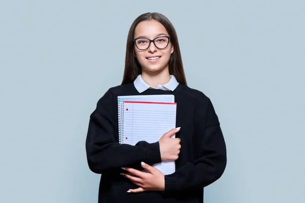 Portrait of teenage female student with backpack notebooks looking at the camera on gray color background. Attractive teen girl in glasses posing in studio. High school, adolescence, study, education