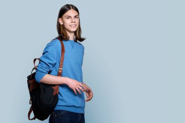 Gri arka planda sırt çantası olan yakışıklı bir gencin portresi. Genç erkek üniversite öğrencisi stüdyoda poz veriyor, fotokopi çekiyor. Eğitim, üniversite, halk, gençlik kavramı