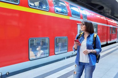 Akıllı telefon sırt çantalı bir kadın istasyon içinde tren istasyonunda bekliyor. Demiryolu taşımacılığı, yolcu taşımacılığı, yolculuk, turizm, seyahat, seyahat, insan konsepti