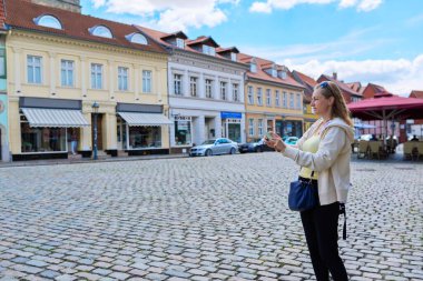 Woman tourist taking photo in an old european city, in front of historical building. Female traveling through Germany using smartphone to take photo. Tourism, history, architecture concept