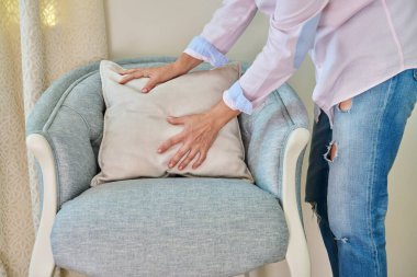 A woman decorating blue armchair with velvet beige cushion. Home interior decoration, style and design, upholstery, furniture concept