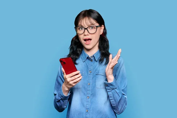 Surprised Teenage Girl Looking Smartphone Screen Blue Color Studio Background — Stok Foto