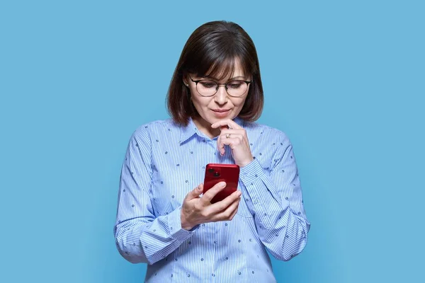 Μεσήλικη Σοβαρή Γυναίκα Ψάχνει Smartphone Μπλε Φόντο Όμορφη Ώριμη Γυναίκα — Φωτογραφία Αρχείου