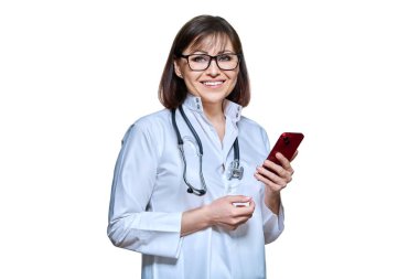 Woman doctor with smartphone looking at camera on white isolated background. Friendly female in uniform with stethoscope phone using mobile apps for work. Medicine technology applications health care