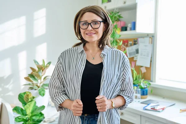 Portrait of confident mature woman looking at camera at home. Middle aged smiling successful female in glasses. 40s age, lifestyle, people concept