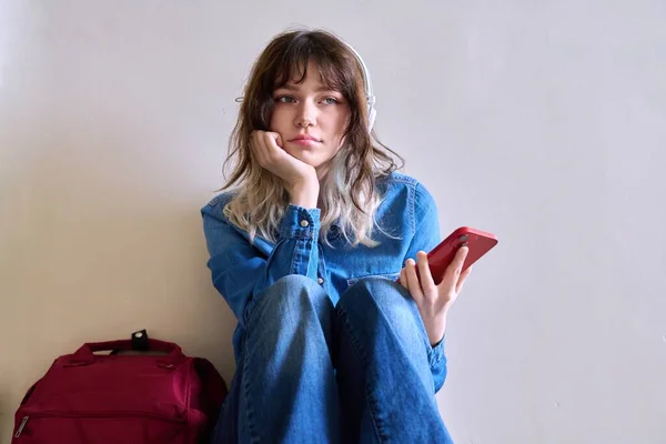 Sad young female student with backpack smartphone sitting near elevator on floor. Lonely frustrated teenage female, frustration problem pain depression concept