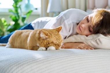 Middle aged woman sleeping with big ginger cat on bed. Mature female owner of old red pet resting with her domestic animal together. Friendship, love, comfort home tranquility, pets, people concept