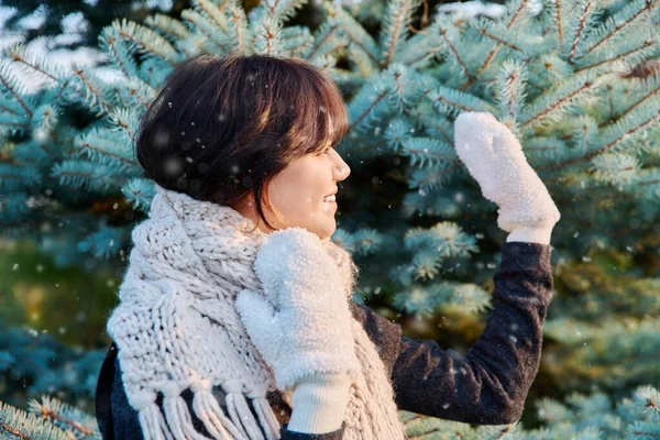 Young woman in scarf mittens looking away waving hand in winter snowy sunny weather, snowflakes on her face in air, near Christmas tree. New Year Christmas holidays concept
