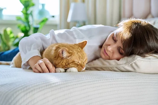 Middle aged woman sleeping with big ginger cat on bed. Mature female owner of old red pet resting with her domestic animal together. Friendship love care comfort home tranquility, pets, people concept