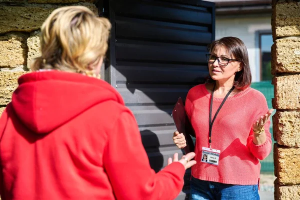 Female social worker talking to a mature woman near gate of house. Social services, visitation and assistance, private practice, insurance, counseling, mental health concept