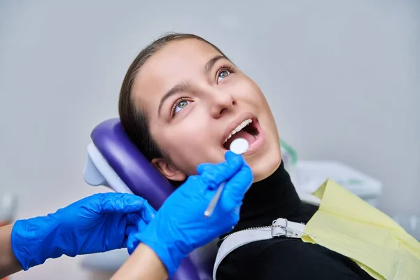 Young teenage female at dental checkup in clinic. Teenage girl sitting in chair, doctor dentist with tools examining patients teeth. Adolescence, hygiene, dentistry, treatment, dental health care