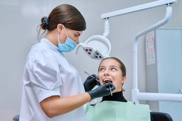 Young teenage female at dental checkup in clinic. Teenage girl sitting in chair, doctor dentist with tools examining patients teeth. Adolescence, hygiene, dentistry, treatment, dental health care