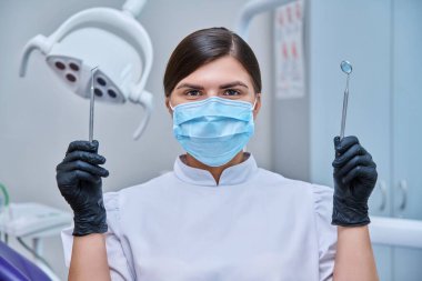 Dişleri incelemek için yüz maskesi takan kadın dişçinin portresi. Doktor kameraya bakıyor, dişçi muayenehanesinde poz veriyor. Diş sağlığı, ilaç, tedavi, diş sağlığı