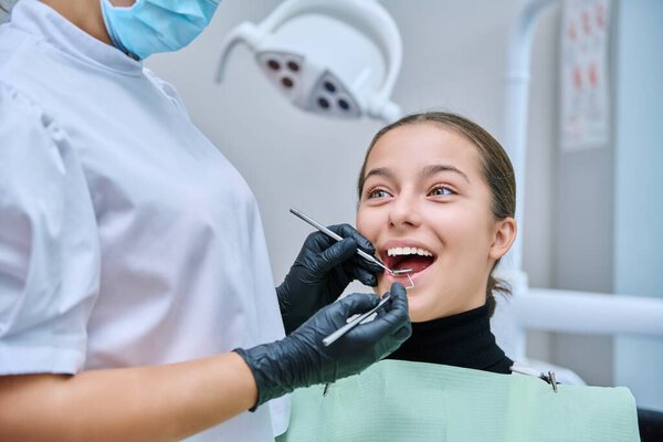 Young teenage female at dental checkup in clinic. Teenage girl sitting in chair, doctor dentist with tools examining patients teeth. Adolescence, hygiene, dentistry, treatment, dental health care