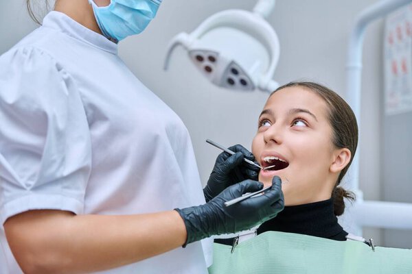 Young teenage female at dental checkup in clinic. Teenage girl sitting in chair, doctor dentist with tools examining patients teeth. Adolescence, hygiene, dentistry, treatment, dental health care