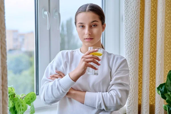 Tonårstjej Med Ett Glas Vatten Med Citron Tittar Kameran Hemma — Stockfoto