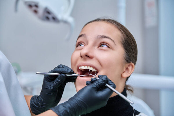 Young teenage female at dental checkup in clinic. Teenage girl sitting in chair, doctor dentist with tools examining patients teeth. Adolescence, hygiene, dentistry, treatment, dental health care