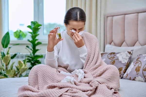 若い10代の女性は鼻水薬のスプレードロップでベッドに座って 組織にくしゃみをし 彼女の鼻を埋める 秋の冬鼻炎鼻水ムッと鼻 インフルエンザの季節 — ストック写真