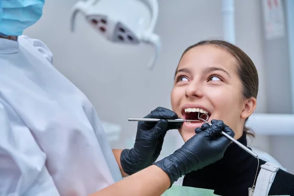 Young teenage female at dental checkup in clinic. Teenage girl sitting in chair, doctor dentist with tools examining patients teeth. Adolescence, hygiene, dentistry, treatment, dental health care