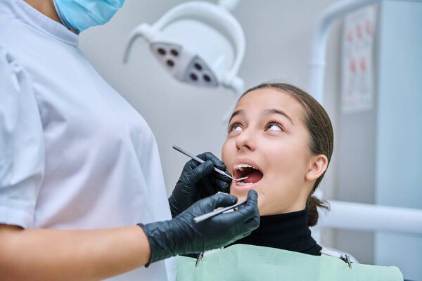 Young teenage female at dental checkup in clinic. Teenage girl sitting in chair, doctor dentist with tools examining patients teeth. Adolescence, hygiene, dentistry, treatment, dental health care