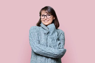 Kendine güvenen orta yaşlı bir kadının portresi pembe renkli stüdyo arkaplanındaki kameraya bakıyor. Kış süveteri örmüş olgun bir kadın. Güzellik, kış mevsimi, kış mevsimi, 40 'ların insanları konsepti.