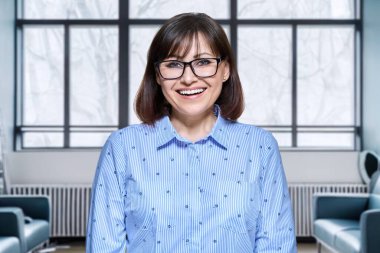 Modern ofis içinde kameraya bakan olgun bir iş kadınının portresi. Olumlu gülümseyen orta yaşlı kadın yönetici patron. İş, banka çalışanı, güven, kariyer, insan konsepti