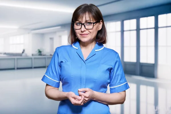 Portrait of confident female nurse inside hospital. Serious middle aged medic doctor looking at camera in reception hall. Medicine, staff, health care, health service, nhs concept