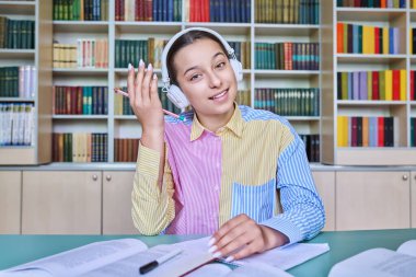 Kütüphanede okuyan genç kız öğrenci. Kulaklıklı bir kadın kameraya bakıyor, not defterine not alıyor. Ergenlik, bilgi, eğitim, lise konsepti