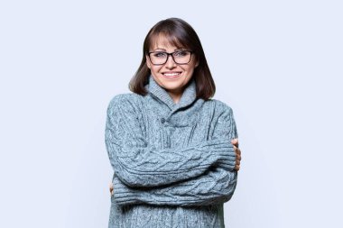 Hafif stüdyo arka planında kameraya bakan kendinden emin orta yaşlı bir kadının portresi. Çapraz kollu, kalın kazaklı olgun bir kadın. Güzellik, soğuk mevsim kış mevsimi, 40 'lı yılların insanları