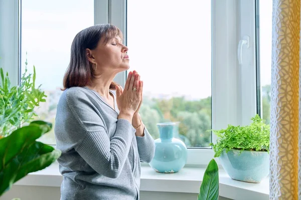 Μεσήλικη Σοβαρή Γυναίκα Προσεύχεται Κοντά Στο Παράθυρο Στο Σπίτι Ώριμο — Φωτογραφία Αρχείου