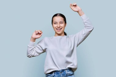 Gri stüdyo geçmişinde neşeli dans eden genç kız. Dans müziğinden hoşlanan mutlu genç bir bayan. Eğlence, ifade, eğlence, mutluluk, başarı, zafer, eğlence, iyi ruh hali konsepti