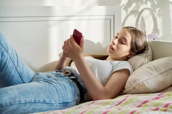 침대에 점심을 소녀가 대화를 스마트폰을 사용하고 소녀가 침실에서 전화로 문자를 — 스톡 사진