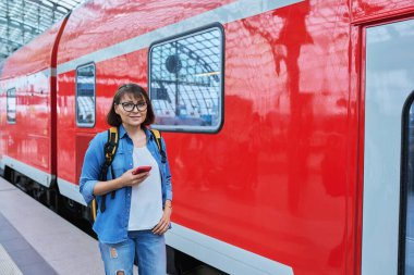 Modern tren istasyonunda şehir demiryolu taşımacılığı yapan kadın yolcu. Akıllı telefonu olan bir kadın, elektrikli tren tarifeli bir web sayfası, online bilet servisi, mobil uygulama üzerinden seyahat için ödeme