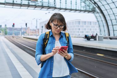 Modern tren istasyonunda şehir demiryolu taşımacılığı yapan kadın yolcu. Akıllı telefonu olan bir kadın, elektrikli tren tarifeli bir web sayfası, online bilet servisi, mobil uygulama üzerinden seyahat için ödeme