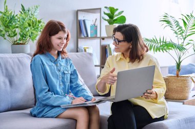 Ergenlik çağındaki kızın çocuğu ve öğretmeninin bireysel dersi. Orta yaşlı bir kadın çocuğa ders veriyor, dizüstü bilgisayar kullanıyor, öğrenci not defterine not alıyor. Bilgi eğitimi, okul öğrenimi, çocukluk konsepti.