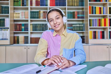Kütüphanede okuyan genç kız öğrenci. Kulaklıklı bir kadın kameraya bakıyor, not defterine not alıyor. Ergenlik, bilgi, eğitim, lise konsepti