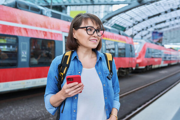 Woman passenger of urban rail transport at modern train station. Female with smartphone, web page with schedule of electric trains, online ticket service, payment for travel through mobile application